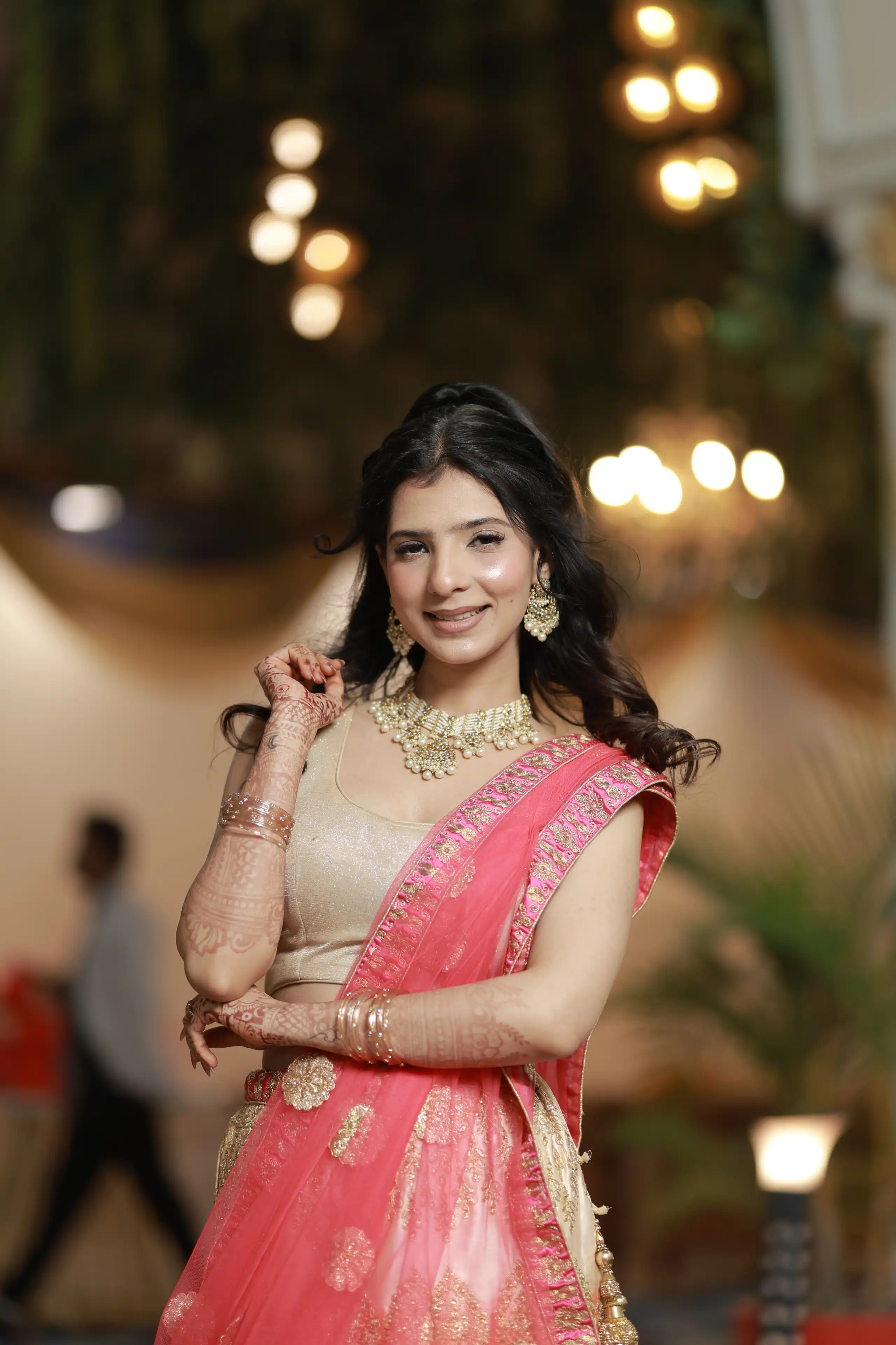 Radiant smiling client in a pink and gold embroidered lehenga with glowing soft makeup and natural wavy hair